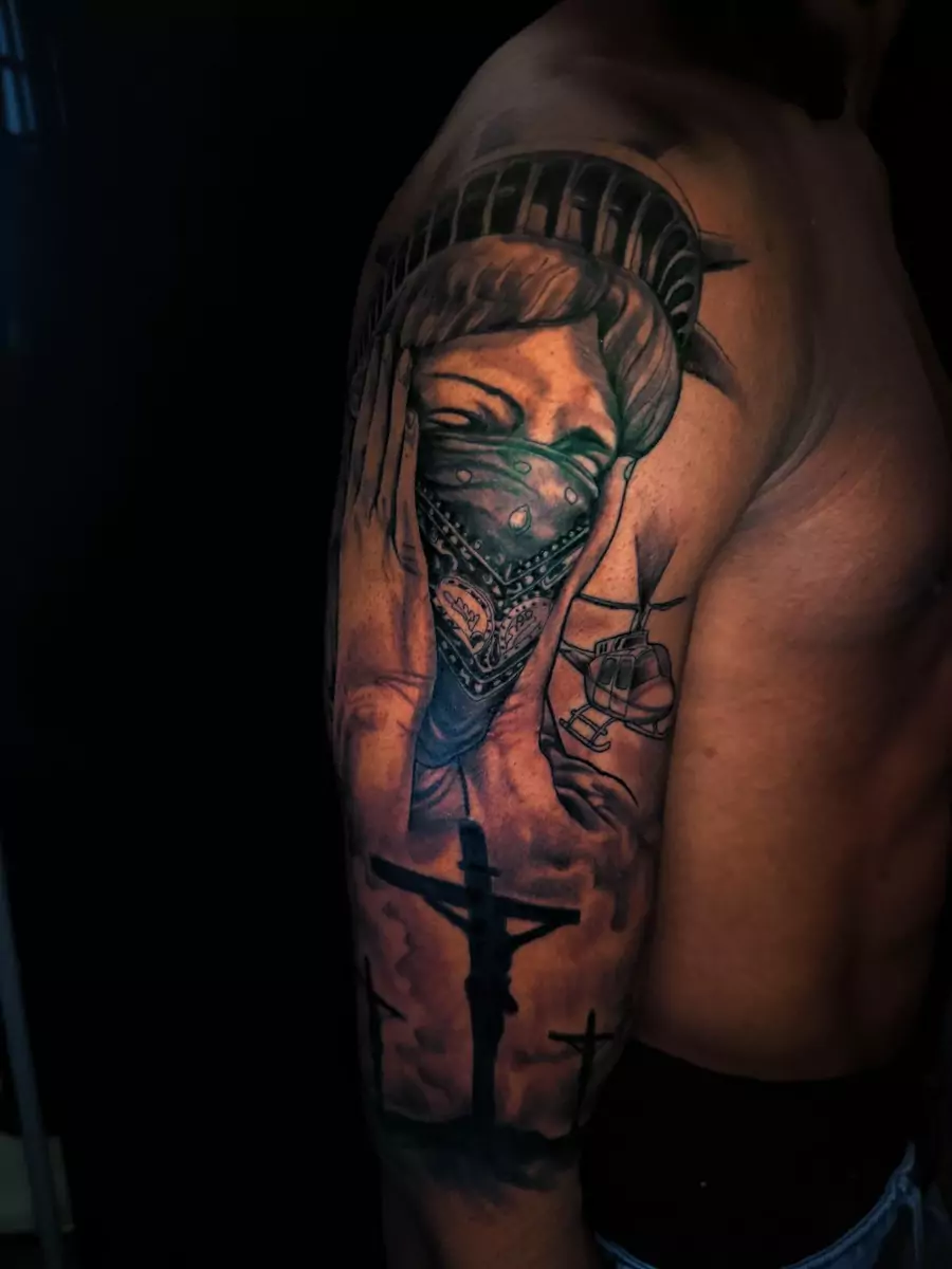 A color shoulder piece of the Statue of Liberty wearing a bandana over her face, with a crucifix below it