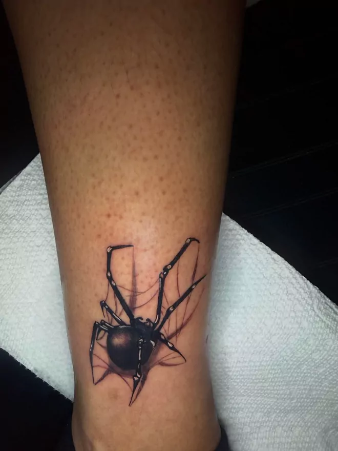 The finished black widow, stencil wiped away, every web line thread-thin against the skin